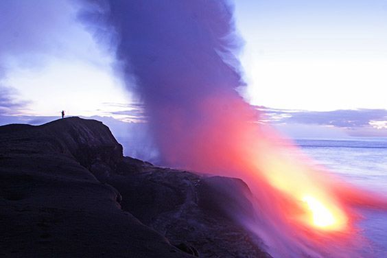 A lone man along the eastern slope of Kilauea Volcano watches as lava pours into the Pacific Ocean, causing the sea to boil into a giant steam cloud.