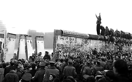 East Germans pour through the Berlin Wall in 1989 as a West Berliner cheers them on from atop.